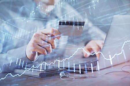 Double exposure of man hands holding a credit card and Forex graph drawing. Stock trading and...