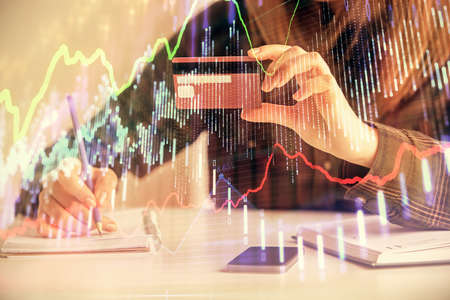 Double exposure of woman on-line shopping holding a credit card and financial graph drawing. Stock...