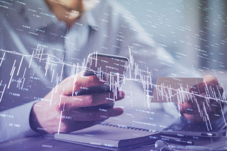 Double exposure of mans hands holding and using a phone and financial graph drawing. Analysis...