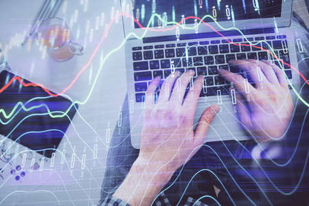 Double exposure of mans hands typing over laptop keyboard and forex chart hologram drawing. Top...