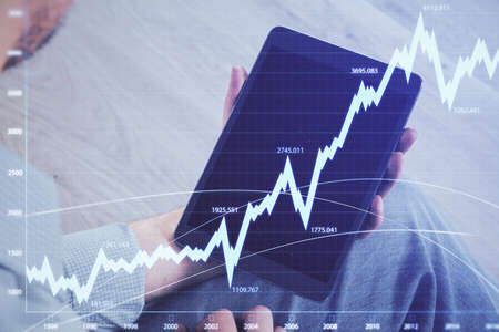 Double exposure of mans hands holding and using a digital device and forex graph drawing. Financial...