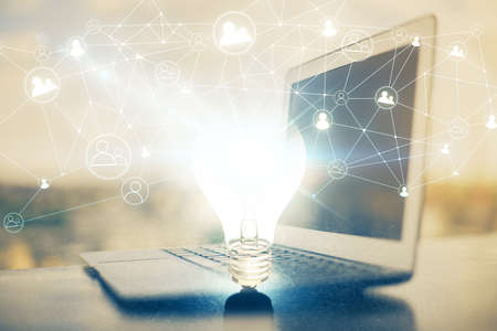 Computer on desktop in office with bulb icon hologram. Double exposure. Concept of idea.