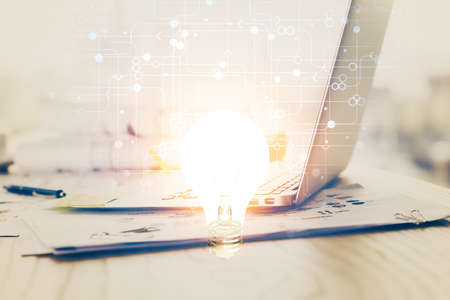 Computer on desktop in office with bulb icon hologram. Double exposure. Concept of idea.の写真素材