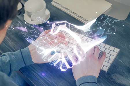 Handshake hologram drawing with businessman working on computer on background. Double exposure.