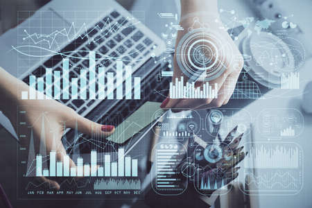 Double exposure of businesswoman hands typing on computer and financial graph hologram drawing....