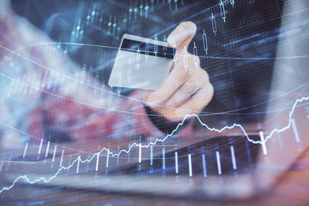 Double exposure of man hands holding a credit card and Forex graph drawing. Stock trading and...