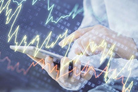 Double exposure of mans hands holding and using a digital device and forex graph drawing. Financial...