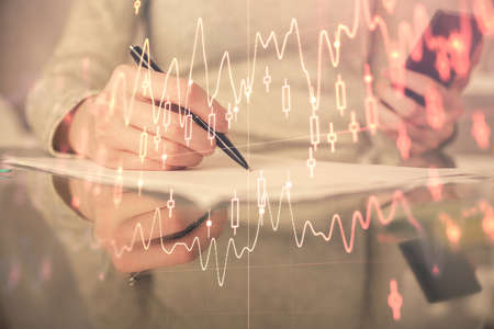 Double exposure of forex chart sketch hologram and woman holding and using a mobile device. Financial market concept.の写真素材