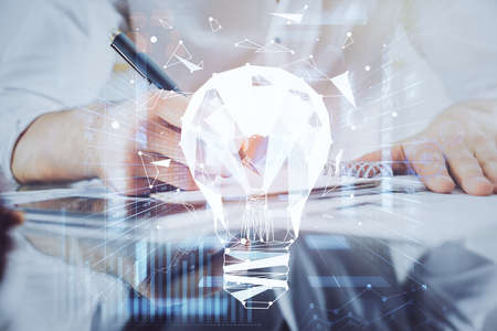 View of Bulb lamp idea concept icon on a futuristic interface with writing mans hand background....