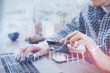 Double exposure of man hands holding a credit card and Forex graph drawing. Stock trading and...
