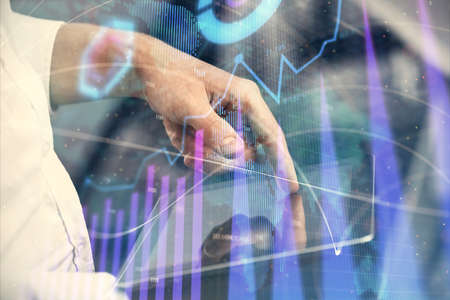 Double exposure of mans hands holding and using a digital device and forex graph drawing. Financial...