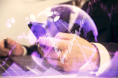 Multi exposure of mans hands holding and using a digital phone and forex graph drawing. Financial...