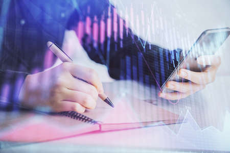 Double exposure of forex graph sketch hologram and woman holding and using a mobile device. Stock...