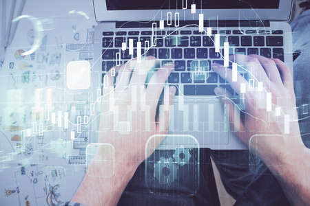 Double exposure of mans hands typing over laptop keyboard and forex chart hologram drawing. Top...