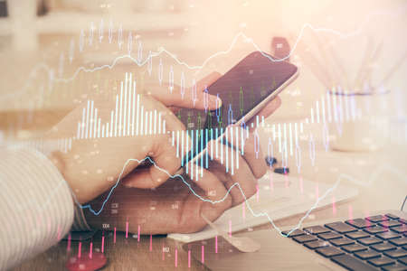 Double exposure of mans hands holding and using a digital device and forex graph drawing. Financial...
