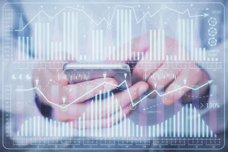 Double exposure of mans hands holding and using a digital device and forex graph drawing. Financial...