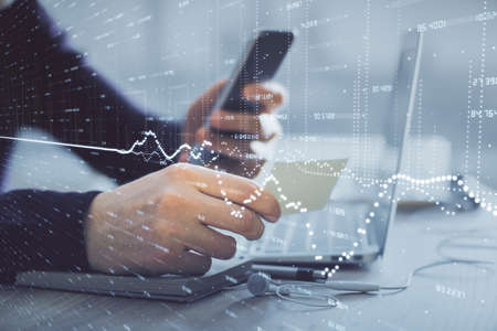 Double exposure of mans hands holding and using a phone and financial graph drawing. Analysis...