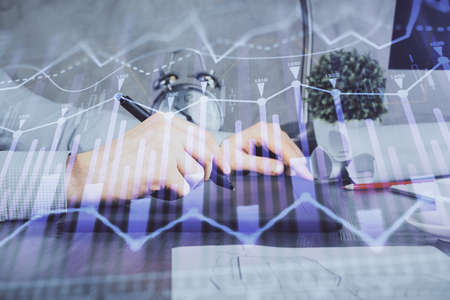 Double exposure of mans hands holding and using a phone and financial graph drawing. Analysis...