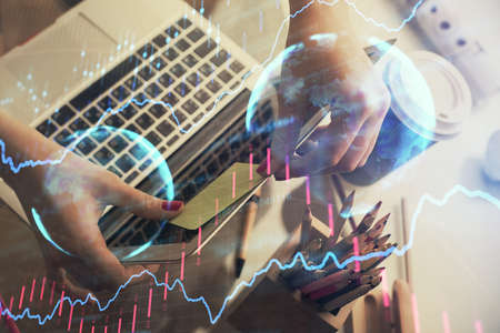 Double exposure of businesswoman hands typing on computer and financial graph hologram drawing....