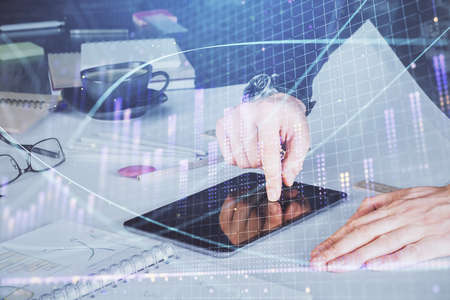 Double exposure of mans hands holding and using a digital device and forex graph drawing. Financial...