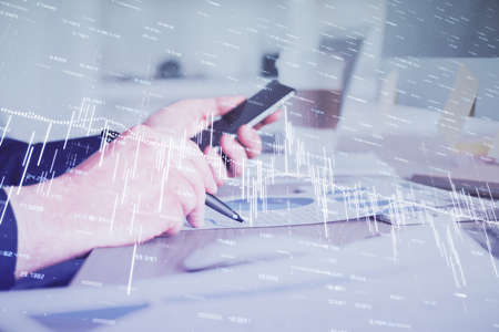 Double exposure of mans hands holding and using a phone and financial graph drawing. Analysis...