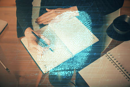 Blue fingerprint hologram over womans hands taking notes background. Concept of protection. Double exposureの写真素材