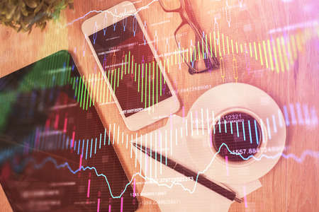 Double exposure of forex chart hologram over the desktop with the phone. Top view. Mobile trade...
