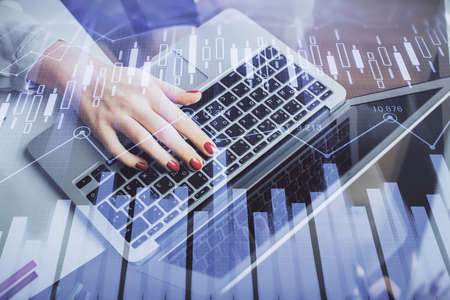 Double exposure of businesswoman hands typing on computer and financial graph hologram drawing....