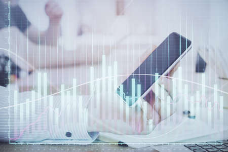 Double exposure of mans hands holding and using a digital device and forex graph drawing. Financial...