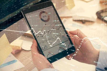 Double exposure of mans hands holding and using a phone and financial graph drawing. Analysis...
