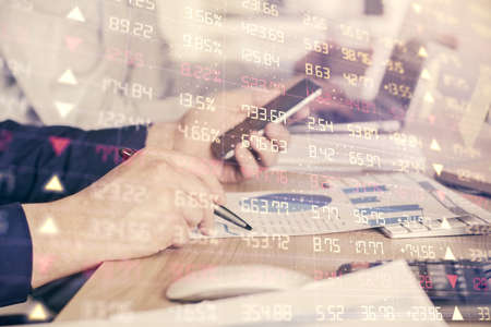 Double exposure of mans hands holding and using a digital device and forex graph drawing. Financial...