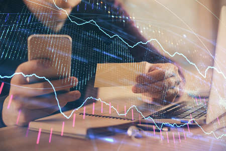 Double exposure of mans hands holding and using a phone and financial graph drawing. Analysis...