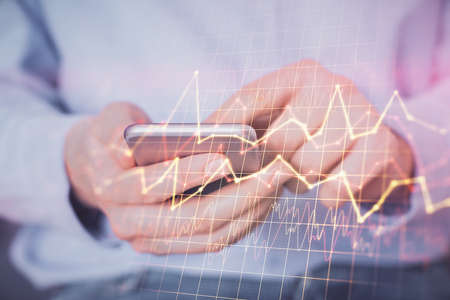 Double exposure of mans hands holding and using a digital device and forex graph drawing. Financial...