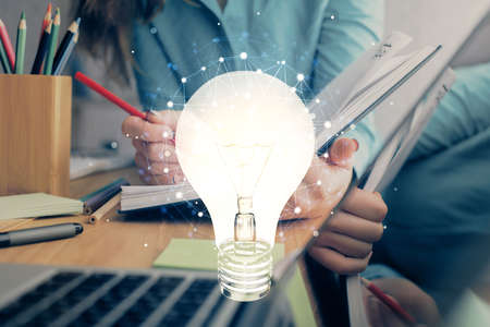 Bulb hologram over hands taking notes background. Concept of idea. Double exposure