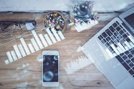 Double exposure of financial graph hologram over desktop with phone. Top view. Mobile trade platform concept.の写真素材