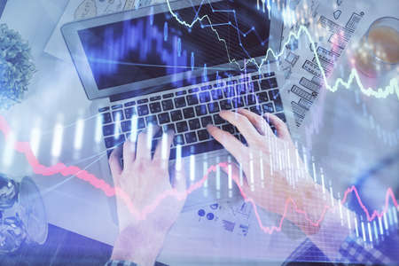 Double exposure of mans hands typing over laptop keyboard and forex chart hologram drawing. Top...
