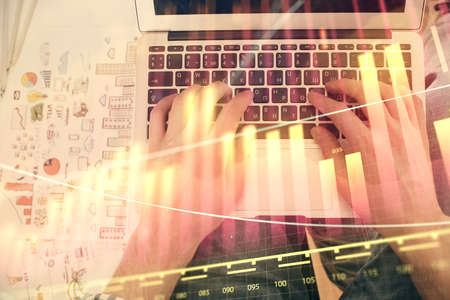 Double exposure of mans hands typing over laptop keyboard and forex chart hologram drawing. Top...