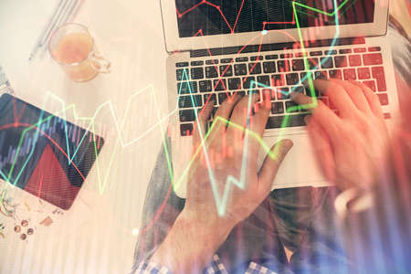 Double exposure of mans hands typing over laptop keyboard and forex chart hologram drawing. Top...