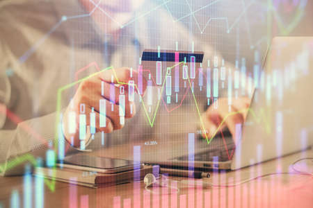 Double exposure of man hands holding a credit card and Forex graph drawing. Stock trading and...