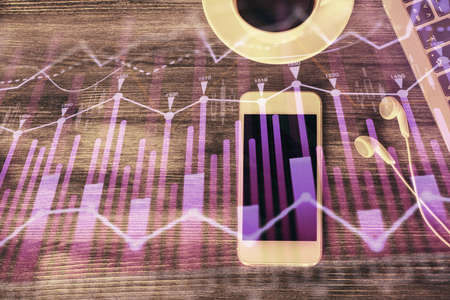 Double exposure of forex chart hologram over desktop with phone. Top view. Mobile trade platform concept.の写真素材
