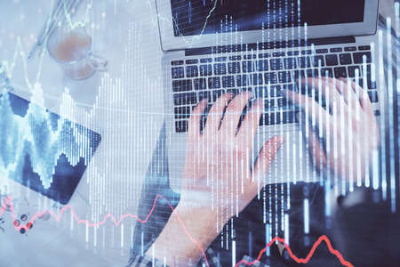 Double exposure of mans hands typing over laptop keyboard and forex chart hologram drawing. Top...