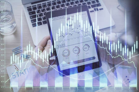 Double exposure of mans hands holding and using a digital device and forex graph drawing. Financial...