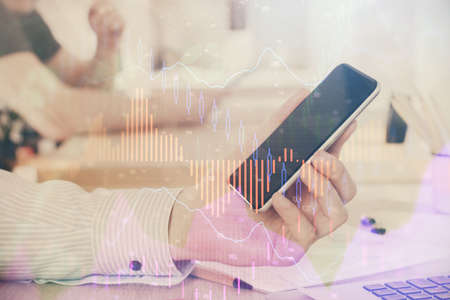 Double exposure of mans hands holding and using a digital device and forex graph drawing. Financial...