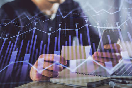 Double exposure of mans hands holding and using a phone and financial graph drawing. Analysis...