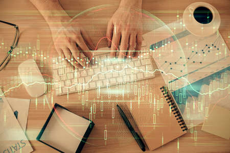 Multi exposure of mans hands typing over computer keyboard and forex graph hologram drawing. Top...