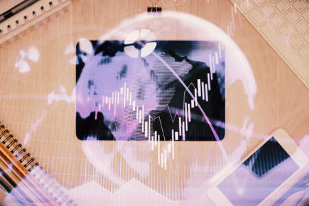 Double exposure of forex graph hologram over desktop with phone. Top view. Mobile trade platform...
