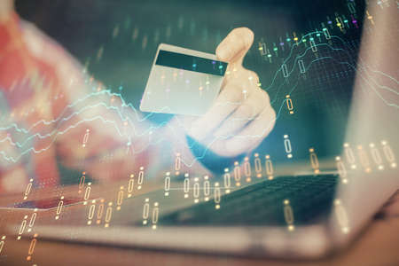 Double exposure of man hands holding a credit card and Forex graph drawing. Stock trading and...
