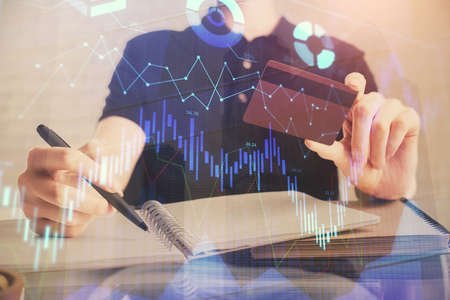 Double exposure of man hands holding a credit card and Forex graph drawing. Stock trading and...