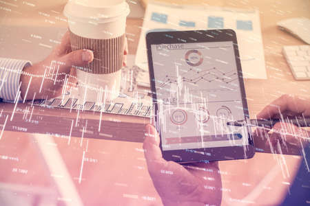 Double exposure of mans hands holding and using a phone and financial chart drawing. Market analysis...