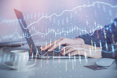 Double exposure of businesswoman hands typing on computer and forex graph hologram drawing....